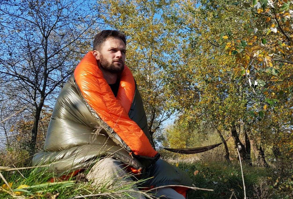 - Cilvēks zem kokiem, ietinies apelsīnu un zaļā krāsā Bushmen GLOW zoss dūnu hamaka sega Bushmen