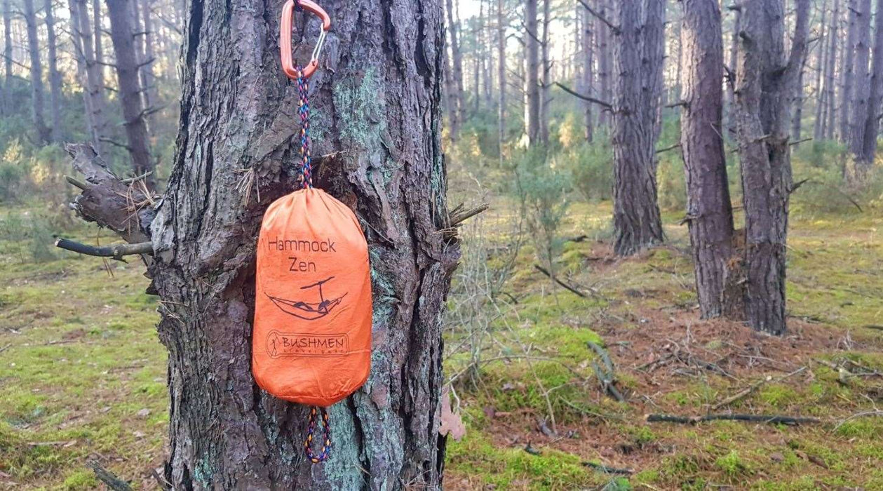 - Bushmen ZEN lightest Hammock oranžā iepakojumā, pievienots koka stumbram mežā
- Bushmen