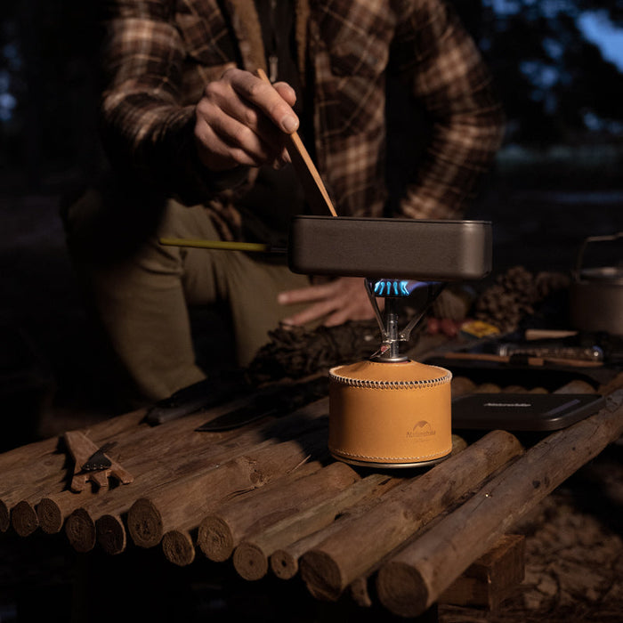 - Kempings uz galda ar Naturehike Ultralight Backpacking Stove Pro Trekking 51gr gāzes plīti, kas gatavo ēdienu dabā vakara laikā ar cilvēku gatavošanas laikā. Naturehike