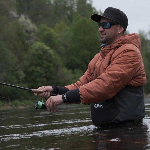 - Vīrietis stāvot ūdenī, turot makšķeri, valkā apelsīnu dūnu jaku un Outfish neoprēna aproces, Outfish