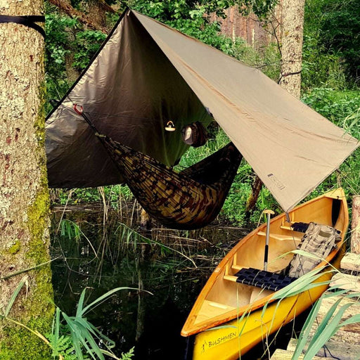 - Bushmen THERMO Hammock Tarp 3×3 / Olive 750g uzstādīts starp diviem kokiem,
- Olīvkrāsas termoaizsargs pārklāj šūpuli, kas karājas virs ūdens,
- Dzeltena laiva Bushmen klāt ūdenstilpnē,
- Viegls, ūdensizturīgs, un ļoti izturīgs audums ar ripstop aušanas,
- Bushmen,