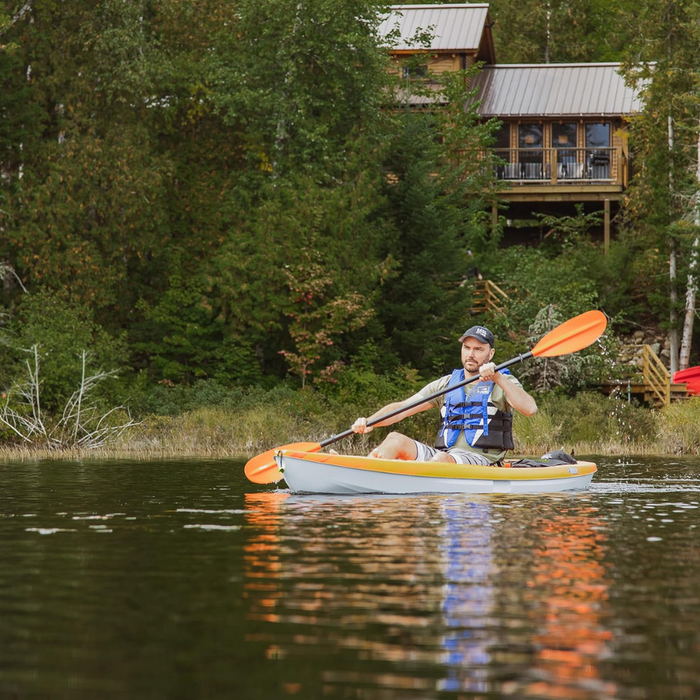 - Vīrietis airējot ar "Recreational Kayak Sit on Top Pelican Sentinel 100x" uz ūdens, apkārt zaļa meža ainava, redzams uzvelkts drošības vesti.
- Outfish