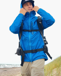 Lietus jaka zila vīrietim kurš iet ar mugusromu gar jūras piekrasti