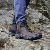 Pārgājienu zābaki Alpina Prima Mid Classic brūns nubuks uz kājām cilvēkam, kurš iet pa ceļu